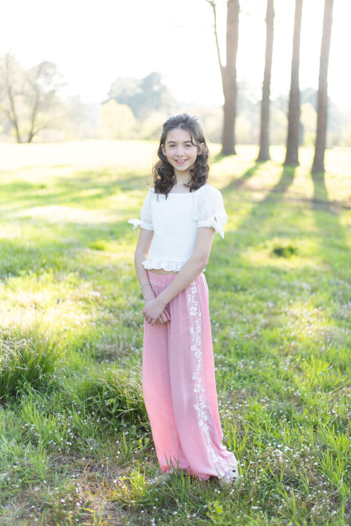 older girl standing in a field in pink pants and white shirt. spring family photos in birmingham al