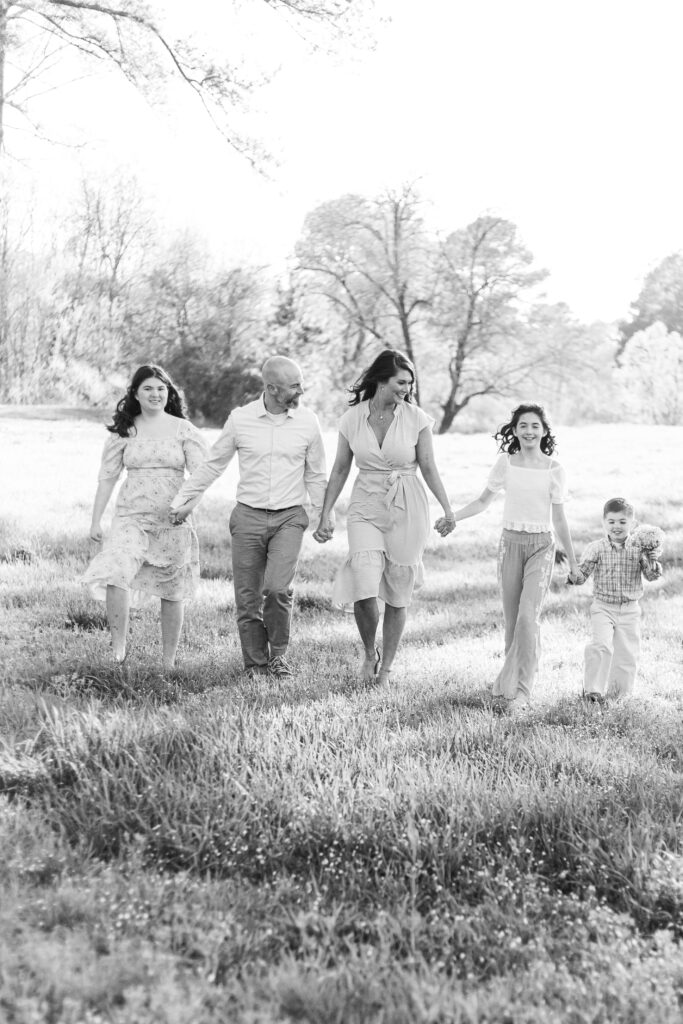 black and white photo of a family of 5 walking in a field and holding hands