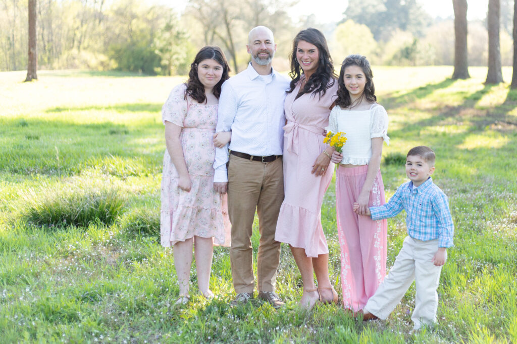 Family of 5 standing in a field in Birmingham, Alabama for spring photo session.  Wearing spring outfits and holding flowers.