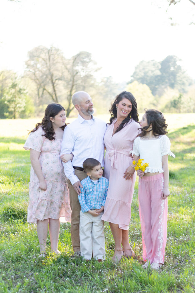 Family standing in a field for a photo session in Birmingham, Alabama.  Light pink outfits, with a little boy in blue.